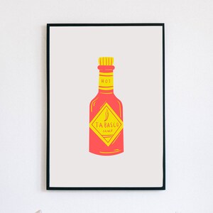 May include: A framed print of a red and yellow illustration of a Tabasco hot sauce bottle. The bottle has a yellow label with the words "Tabasco Sauce" and a red chilli pepper.
