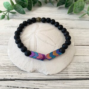 May include: A black lava rock bracelet with a gold bead and iridescent arrow charm.