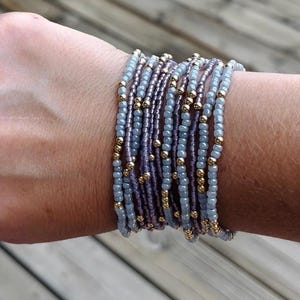 May include: A collection of beaded bracelets in shades of blue, purple, and gold. The bracelets are made of small beads strung together, creating a layered effect. The gold beads add a touch of sparkle.