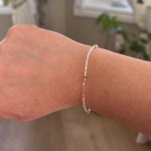 Peut inclure: Un bracelet délicat composé de perles rectangulaires transparentes, assemblées avec des accents dorés. Le bracelet est porté sur un poignet, mettant en valeur son design minimaliste et son élégance subtile. Les perles mesurent environ 0,25 cm.