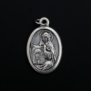 Puede incluir: Pendiente de plata con una imagen en relieve de una mujer sosteniendo un paño con el rostro de un hombre.