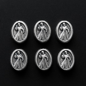 Puede incluir: Seis dijes de metal plateados con una imagen religiosa de un hombre con los brazos extendidos. Los dijes est&aacute;n dispuestos en dos filas de tres sobre un fondo negro.