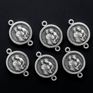 May include: Six silver-toned Holy Family medallions. Each circular pendant features an embossed image of a family and the words "HOLY FAMILY" and "ITALY". The medallions have small loops for attaching to a chain or other jewelry.