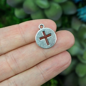 May include: Silver charm with a cross cut-out. The cross is red and the charm has a textured surface.