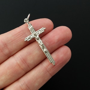 Op de afbeelding: Zilveren kruis hanger met een gedetailleerd figuur van Jezus Christus. Het kruis heeft een eenvoudig, elegant ontwerp met meerdere lijnen die in het midden lopen.