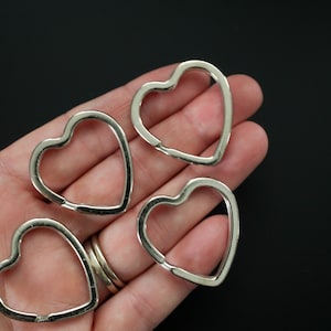 May include: Four silver heart-shaped key rings. The key rings are shown in a hand, with the rings facing the camera.
