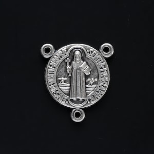 Puede incluir: Encanto de metal plateado con una representación de San Antonio de Padua. El encanto tiene una forma circular con una imagen en relieve del santo sosteniendo un bebé Jesús y un lirio. La inscripción alrededor de la imagen dice "S. Antonius de Padua" y "Ora pro nobis". El encanto tiene tres pequeños bucles para sujetarlo a un collar o pulsera.