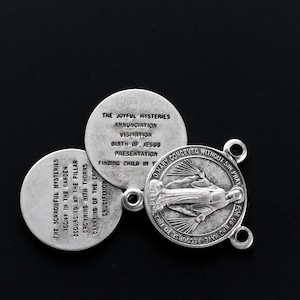 May include: A silver rosary centre and three round medallions. The centre features an image of the Virgin Mary and the text "O Mary conceived without sin, pray for us who have recourse to thee." The medallions list the Joyful and Sorrowful Mysteries.