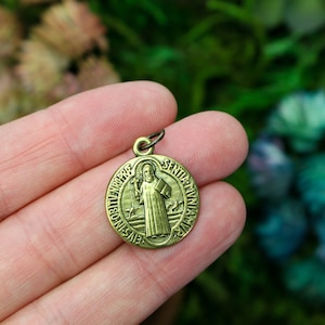 May include: A gold-toned metal pendant depicting Saint Anthony of Padua. The pendant is circular and inscribed with the words "S. Antonius Padua" and "Ora Pro Nobis".