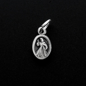 May include: Silver charm featuring a depiction of Jesus Christ with rays of light emanating from his chest. The charm is oval shaped and has a loop at the top for attaching to a necklace or bracelet.