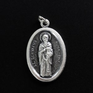 May include: Silver oval pendant with a depiction of a saint holding a book. The pendant has the text "ST. SERVATUS" and "LOTAR - ITALY" on it.