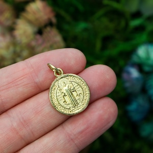 May include: Gold-toned Saint Benedict medal pendant featuring a detailed image of Saint Benedict and a Latin inscription.