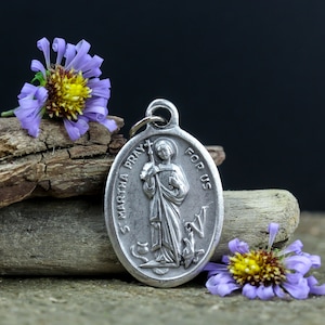 Può includere: Ciondolo in argento con una raffigurazione di Santa Marta in preghiera, circondato da un motivo floreale. Il ciondolo recita "St. Martha Pray For Us".