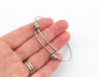 Puede incluir: Un brazalete de plata con un diseño sencillo. El brazalete tiene dos pequeños elementos decorativos redondos a cada lado de la abertura.
