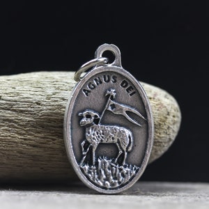 May include: A silver oval pendant with a depiction of a lamb carrying a flag with the words "Agnus Dei" inscribed around the edge.