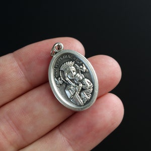 Op de afbeelding: Zilveren ovale hanger met een reli&euml;fbeeld van Onze-Lieve-Vrouw van de Onbevlekte Ontvangenis, een katholiek icoon dat de Maagd Maria met het kind Jezus toont. De hanger heeft de woorden "Onze-Lieve-Vrouw van de Onbevlekte Ontvangenis" rond de rand gegraveerd.