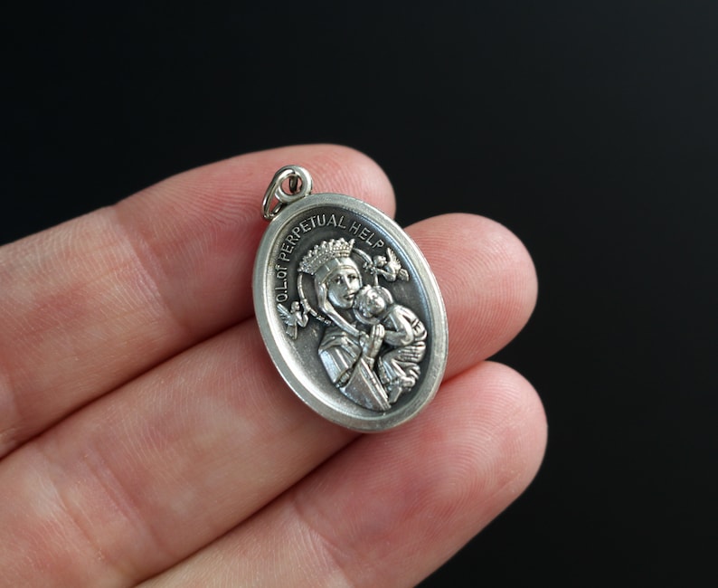 Op de afbeelding: Zilveren ovale hanger met een reli&euml;fbeeld van Onze-Lieve-Vrouw van de Onbevlekte Ontvangenis, een katholiek icoon dat de Maagd Maria met het kind Jezus toont. De hanger heeft de woorden "Onze-Lieve-Vrouw van de Onbevlekte Ontvangenis" rond de rand gegraveerd.