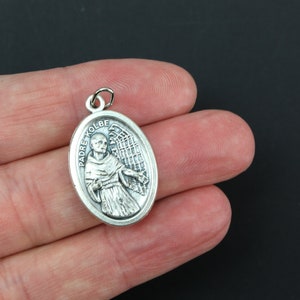 May include: Silver oval pendant with a depiction of Padre Kolbe, a Catholic saint, with an angel's wings behind him.