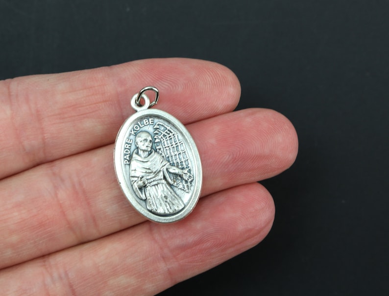 May include: Silver oval pendant with a depiction of Padre Kolbe, a Catholic saint, with an angel's wings behind him.