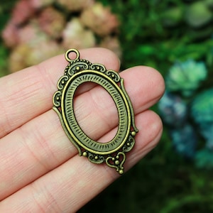 May include: An antique gold oval-shaped metal frame with a decorative design. The frame has a loop at the top for hanging.