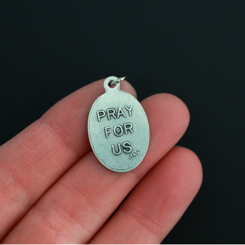 May include: Silver oval pendant with the words "Pray for Us" and "Italy" inscribed on it.