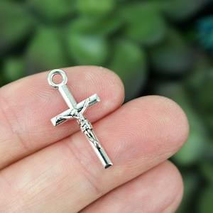 Puede incluir: Un dije de metal plateado en forma de cruz con una figura detallada de Jesucristo. El dije es pequeño y sería adecuado para la elaboración de joyas u otros proyectos de artesanía.
