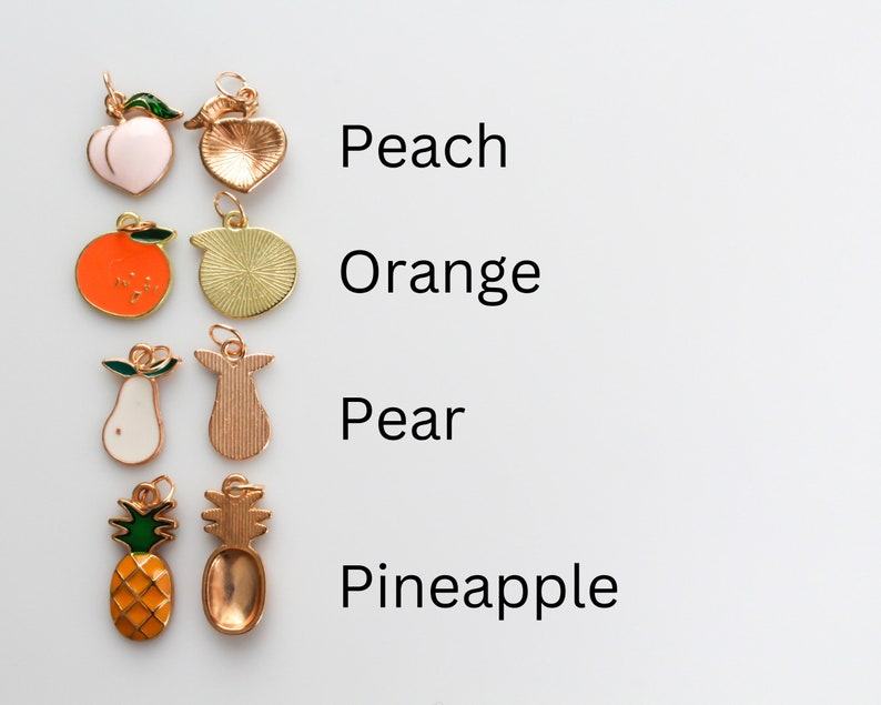 Pu&ograve; includere: Un set di ciondoli dorati a forma di frutta, tra cui una pesca, un'arancia, una pera e un ananas. Ogni ciondolo presenta un design smaltato dettagliato e un anello per attaccarlo a una collana o un braccialetto.