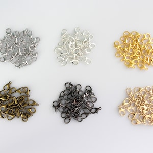 May include: Six piles of metal lobster clasps in different finishes: silver, gold, antique brass, black, and gunmetal. Each pile contains approximately 20 clasps.