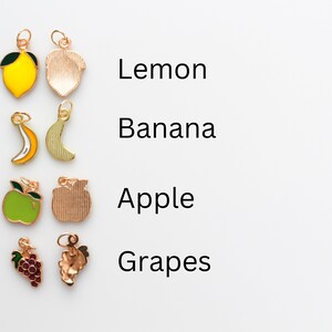 Pu&ograve; includere: Un set di ciondoli in metallo dorato che raffigurano diversi frutti: un limone, una banana, una mela e dell'uva. Ogni ciondolo ha un anello per essere attaccato a una collana, un braccialetto o un altro gioiello.