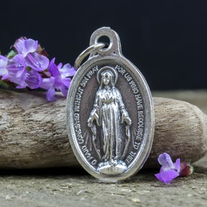 May include: Silver pendant featuring a depiction of the Virgin Mary with the inscription "O Mary Conceived Without Sin Pray For Us Who Have Recourse To Thee".