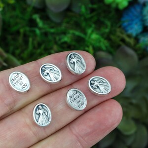 Puede incluir: Seis dijes ovalados de plata con una imagen religiosa de Jes&uacute;s y el texto "Jes&uacute;s conf&iacute;o en ti".
