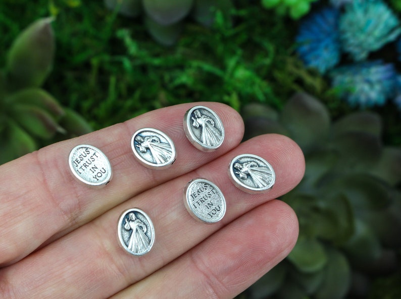 Puede incluir: Seis dijes ovalados de plata con una imagen religiosa de Jes&uacute;s y el texto "Jes&uacute;s conf&iacute;o en ti".