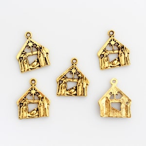 May include: Five gold-colored metal charms shaped like a nativity scene. Each charm features a star, a manger, and figures of Mary, Joseph, and the baby Jesus.