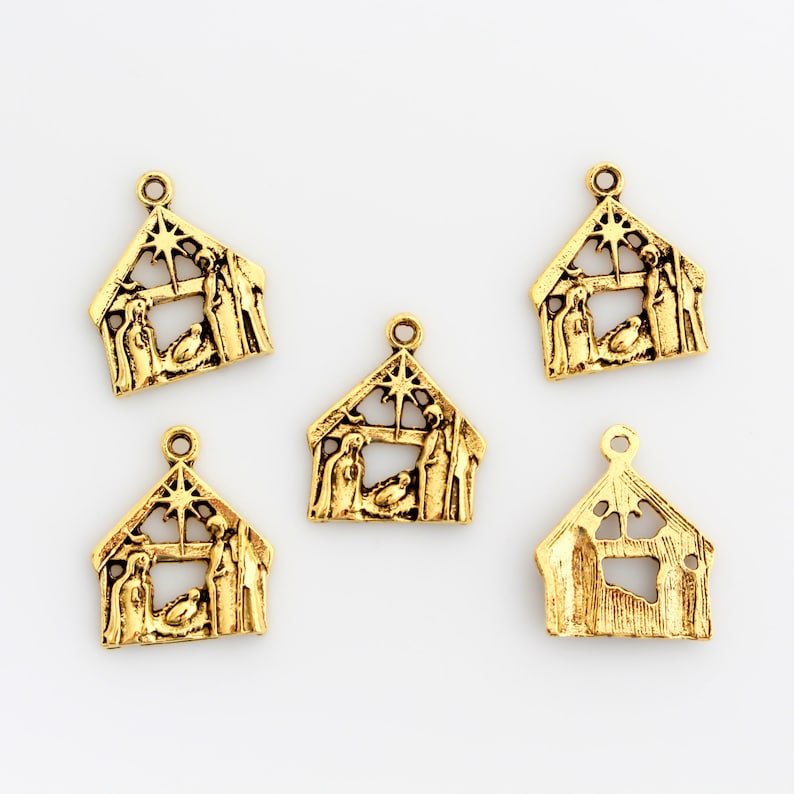 May include: Five gold-colored metal charms shaped like a nativity scene. Each charm features a star, a manger, and figures of Mary, Joseph, and the baby Jesus.
