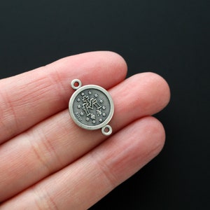May include: Silver-toned metal charm with a round design featuring a religious icon and the letters "Ave Maria".
