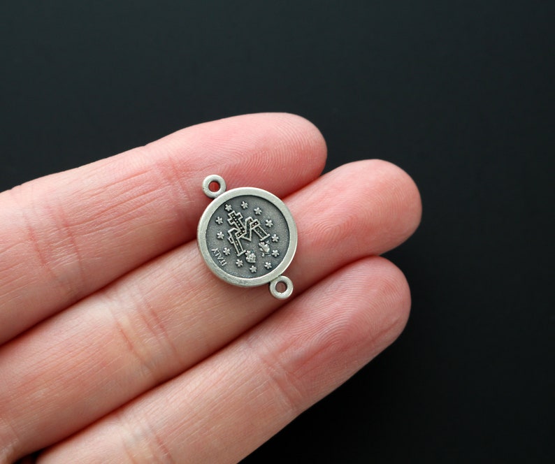 May include: Silver-toned metal charm with a round design featuring a religious icon and the letters "Ave Maria".