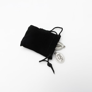 May include: A black velvet pouch with a drawstring closure, containing two silver-toned medallions. One medallion features a depiction of the Virgin Mary, while the other depicts a saint.