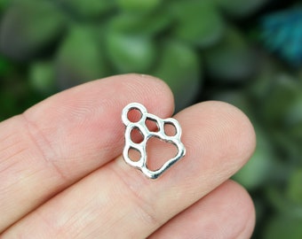 May include: Silver charm in the shape of a paw print. The charm is hollow and has a smooth, shiny finish.