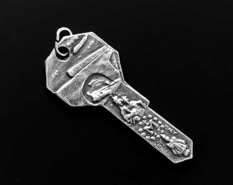 May include: Silver key charm with a detailed design of the Colosseum in Rome, Italy. The charm features a small ring at the top for attaching to a keychain or necklace.