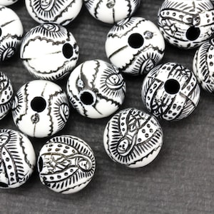 May include: A collection of white wooden beads with black intricate designs. The beads have a hole in the center for stringing.