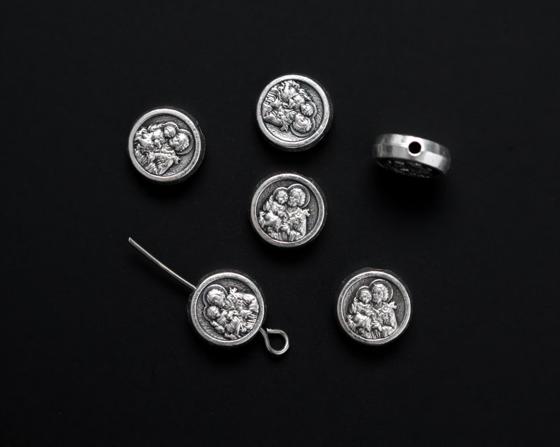 May include: Six silver-toned metal charms with religious imagery. The charms feature a depiction of the Holy Family.