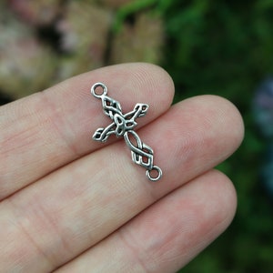 May include: Silver Celtic knot cross charm with two jump rings. The cross is intricately designed with a knot pattern.
