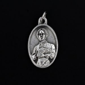 Puede incluir: Pendiente ovalado de plata con una imagen en relieve de una mujer con un cuello blanco y un libro en sus manos.