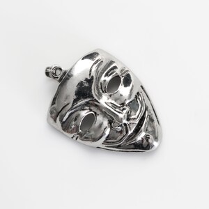 May include: A silver pendant in the shape of a mask with a sinister grin and two eye holes.