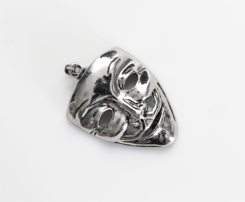 May include: A silver pendant in the shape of a mask with a sinister grin and two eye holes.