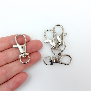 May include: Four silver-toned metal keychains with a swivel clasp. The keychains are in a pile on a white surface.