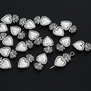 May include: A collection of silver-toned metal heart charms with a flame design. The charms are scattered on a black surface.
