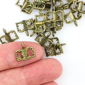 May include: A pile of antique gold-toned metal book charms with a cutout design. The charms have a textured surface and are perfect for adding a vintage touch to jewelry or crafts.