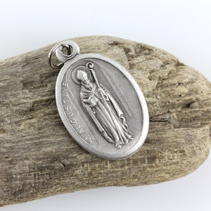 May include: Silver oval pendant with a depiction of Saint Augustine, a Catholic saint, holding a book and a staff. The pendant has the words "St. Augustine" inscribed around the edge.