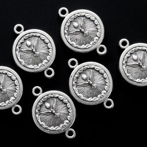 May include: Six silver-toned round charms with a dove and sunburst design. Each charm has two small loops for attaching to other components. The charms are on a black background.